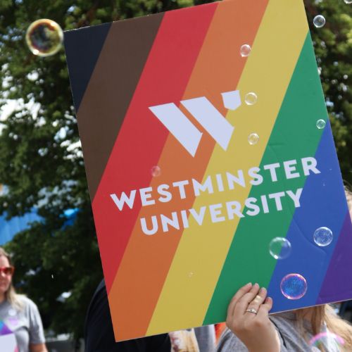 student holding a rainbow striped poster with the Westminsyer University logo